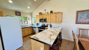 Kitchen with high vaulted ceiling, light brown cabinets, appliances with stainless steel finishes, light tile patterned floors, and a kitchen breakfast bar