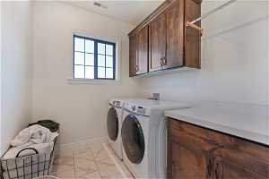 Clothes washing area featuring washing machine and clothes dryer, light tile floors, cabinets, and washer hookup