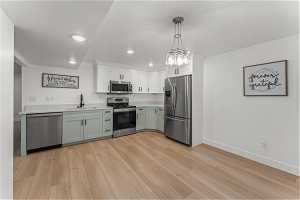 Second Kitchen with hanging light fixtures, stainless steel appliances, a notable chandelier, sink, and light wood-type flooring