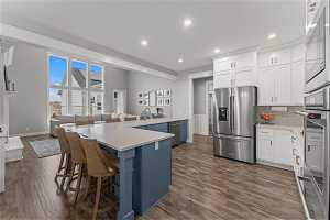 Kitchen featuring a breakfast bar area, appliances with stainless steel finishes, backsplash, dark hardwood / wood-style floors, and white cabinets