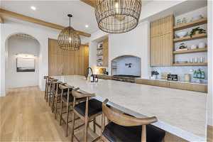 Kitchen with light hardwood / wood-style floors, tasteful backsplash, a breakfast bar area, beam ceiling, and decorative light fixtures