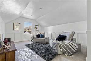 Bedroom with vaulted ceiling, light colored carpet, and a textured ceiling