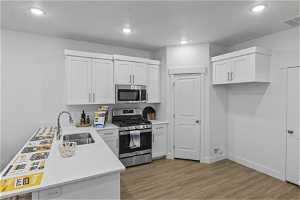 Kitchen with light hardwood / wood-style flooring, white cabinets, sink, and stainless steel appliances
