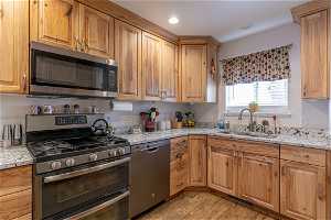 Kitchen featuring sink, stainless steel appliances, light stone counters, and light hardwood / wood-style floors
