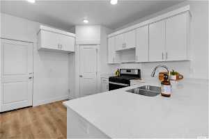 Kitchen with gas range, white cabinets, sink, and light hardwood / wood-style floors