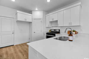 Kitchen with gas range, white cabinets, sink, and light hardwood / wood-style floors