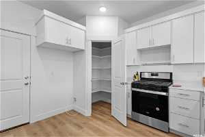 Kitchen with light hardwood / wood-style flooring, white cabinetry, and stainless steel gas range