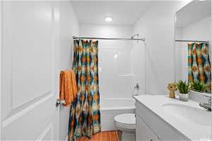 Full bathroom with toilet, large vanity, shower / bathtub combination with curtain, and tile flooring