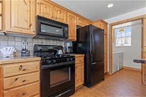 Kitchen featuring black appliances, tasteful backsplash, washer and clothes dryer, and light hardwood / wood-style floors