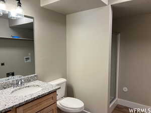 Bathroom with a textured ceiling, oversized vanity, toilet, a shower with shower door, and hardwood / wood-style floors