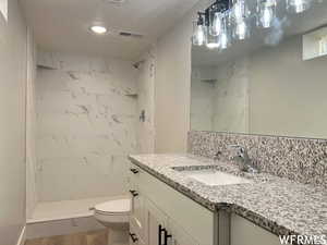 Bathroom featuring toilet, hardwood / wood-style floors, vanity with extensive cabinet space, a tile shower, and a textured ceiling