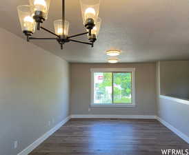 Empty room featuring an inviting chandelier, a textured ceiling, and dark wood-type flooring