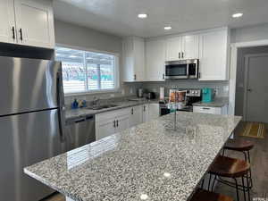 Kitchen featuring stainless steel appliances, white cabinets, a kitchen breakfast bar, and light stone counters