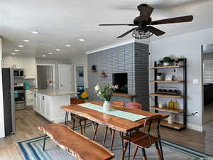 Dining room featuring a tile fireplace, light hardwood / wood-style floors, a textured ceiling, and ceiling fan