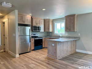 Kitchen featuring light wood-type flooring, light stone counters, stainless steel appliances, and kitchen peninsula