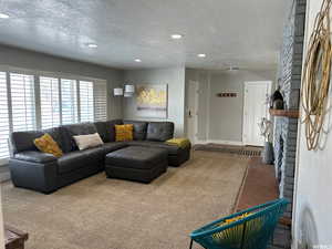 Living room with carpet flooring, a stone fireplace, and a textured ceiling