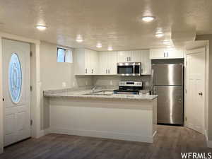 Kitchen with dark hardwood / wood-style floors, white cabinets, stainless steel appliances, and kitchen peninsula