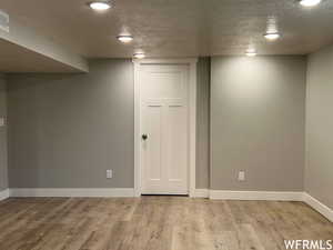 Basement featuring light wood-type flooring and a textured ceiling