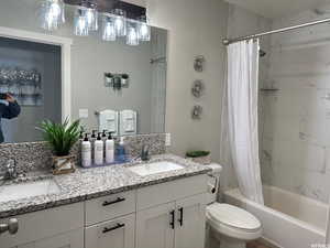 Full bathroom with oversized vanity, double sink, shower / bath combo with shower curtain, and toilet