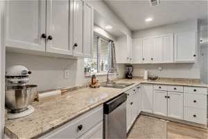 Kitchen with sink, light wood-type flooring, stainless steel dishwasher, and white cabinetry