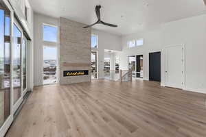 Unfurnished living room featuring light wood-type flooring, a high ceiling, a large fireplace, and ceiling fan