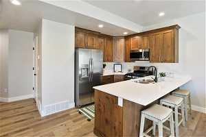 Kitchen with light hardwood / wood-style floors, a breakfast bar, kitchen peninsula, sink, and stainless steel appliances