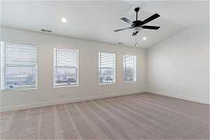 Empty room with light carpet, a healthy amount of sunlight, vaulted ceiling, and ceiling fan
