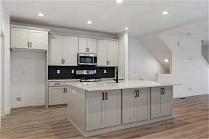 Kitchen with white cabinets, light hardwood / wood-style floors, a kitchen island with sink, and stove