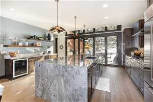 Kitchen featuring beverage cooler, dark stone counters, pendant lighting, sink, and a center island with sink