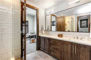 Bathroom featuring vanity with extensive cabinet space, an enclosed shower, tile flooring, and dual sinks