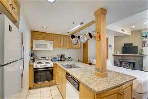 Kitchen with ceiling fan, light tile floors, light stone countertops, white appliances, and sink
