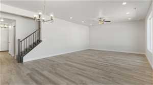 Unfurnished room featuring ceiling fan with notable chandelier and light hardwood / wood-style floors