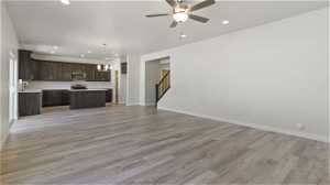 Unfurnished living room with sink, light hardwood / wood-style floors, and ceiling fan with notable chandelier
