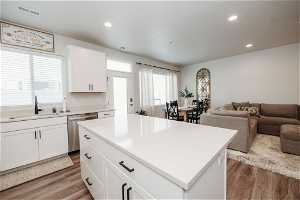 Kitchen featuring stainless steel dishwasher, light hardwood / wood-style flooring, white cabinets, sink, and a center island