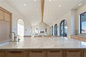 Kitchen with light stone countertops, light brown cabinetry, beam ceiling, sink, and a kitchen island with sink