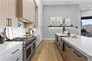 Kitchen with light hardwood / wood-style floors, range with two ovens, tasteful backsplash, light stone counters, and sink