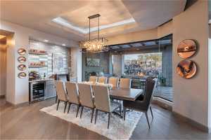 Dining area featuring a chandelier, a raised ceiling, wine cooler, and hardwood / wood-style floors