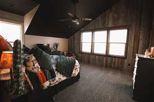 Bedroom featuring wooden walls, vaulted ceiling, carpet floors, and ceiling fan