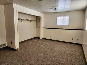 Unfurnished bedroom featuring a closet, a textured ceiling, and dark colored carpet