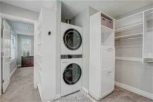 Laundry area featuring stacked washer / dryer and light carpet