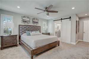 Carpeted bedroom with ensuite bath, a barn door, and ceiling fan