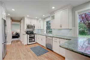 Kitchen with backsplash, stainless steel appliances, light hardwood / wood-style floors, white cabinets, and sink