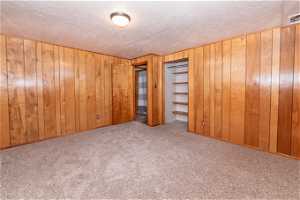 Interior space with a closet, wooden walls, a textured ceiling, and light carpet