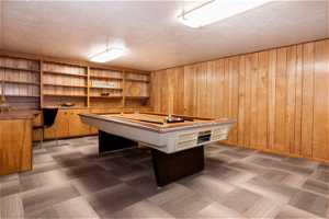 Game room with pool table, wooden walls, and a textured ceiling