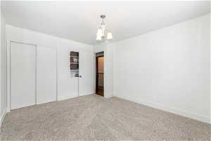 Unfurnished bedroom with light carpet, a chandelier, and a closet