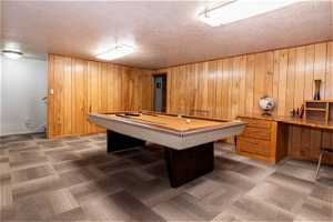 Playroom featuring dark colored carpet, wooden walls, billiards, and a textured ceiling