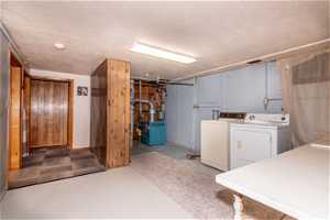 Basement with washing machine and clothes dryer, light carpet, and a textured ceiling