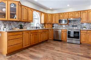 Kitchen with dark hardwood / wood-style flooring, light stone countertops, backsplash, sink, and stainless steel appliances
