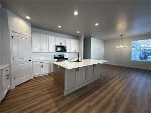 Kitchen with stainless steel appliances, white cabinets, an island with sink, and dark hardwood / wood-style flooring