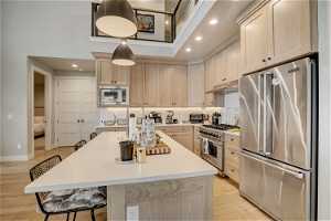 Kitchen with a breakfast bar, a kitchen island with sink, light hardwood / wood-style floors, and premium appliances